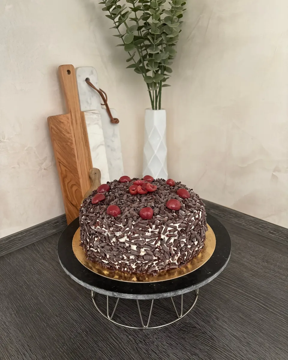 Forêt-noire entièrement masquée de copeaux de chocolat et couronnée de cerises, sur un présentoir sombre.
