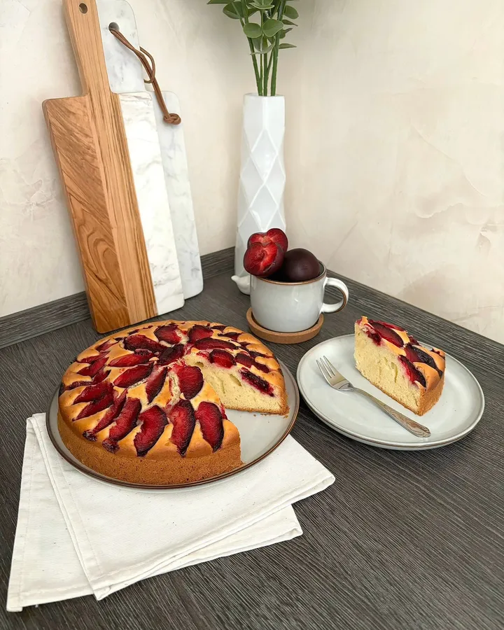 Gâteau aux quartiers de prunes disposés en rosace, une part découpée posée à côté sur une assiette.