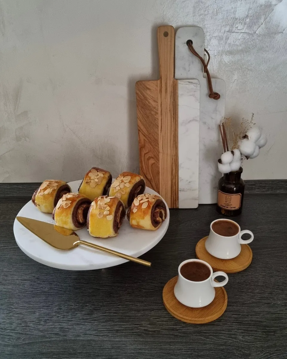 Six roulés bicolores parsemés d'amandes effilées sur un présentoir en marbre, avec une pelle dorée et deux cafés turcs.